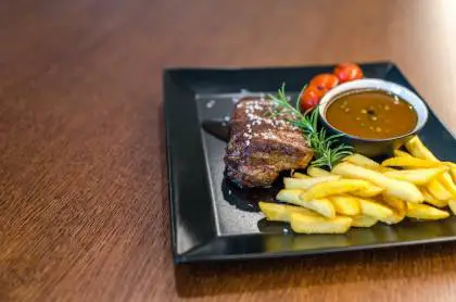 grilled beef with fries and sauce on black ceramic plate
