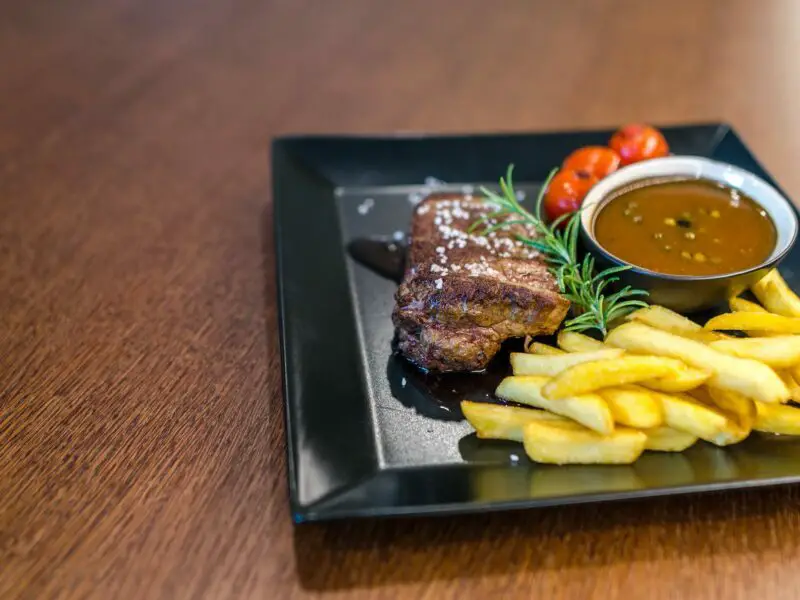 grilled beef with fries and sauce on black ceramic plate